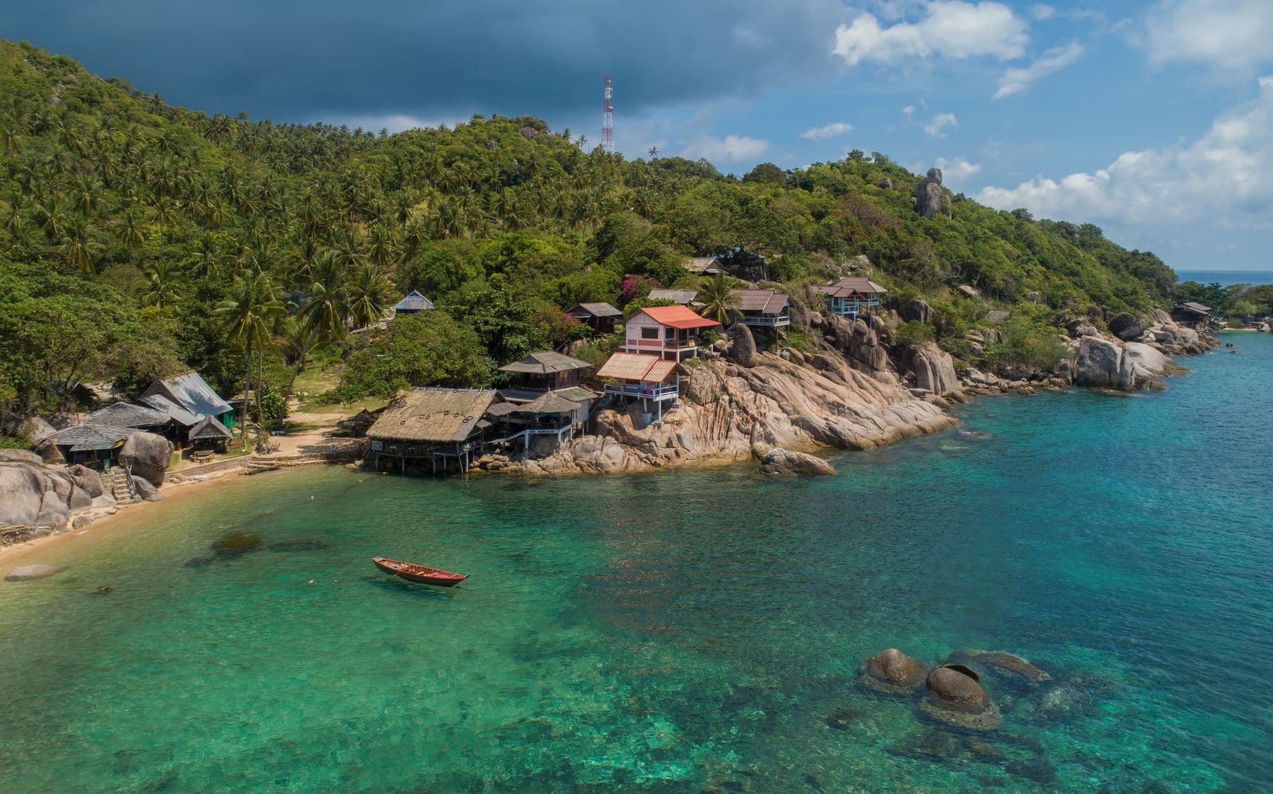 Wooden houses above a rocky bay and turquoise water on Koh Tao