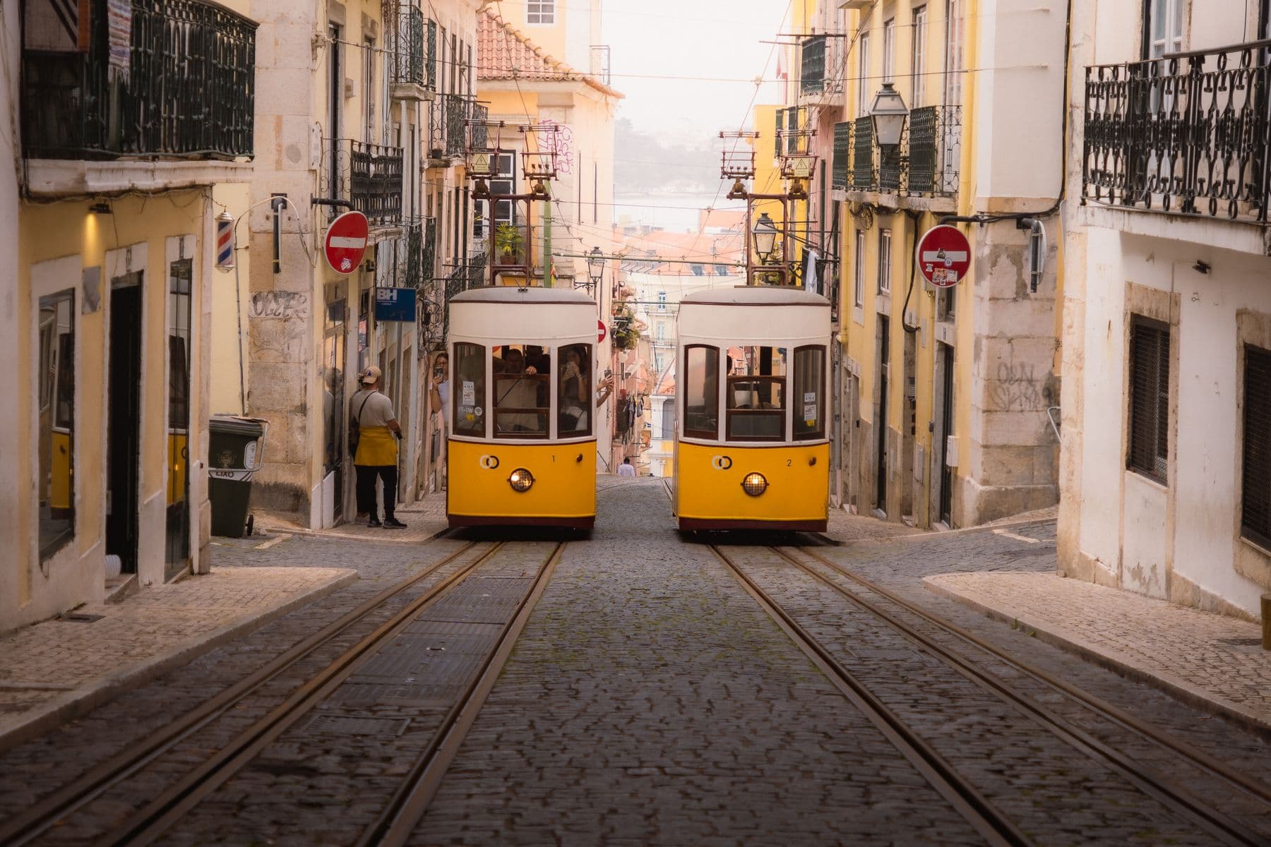 Two yellow trams passing on a cobbled street in Lisbon's old town